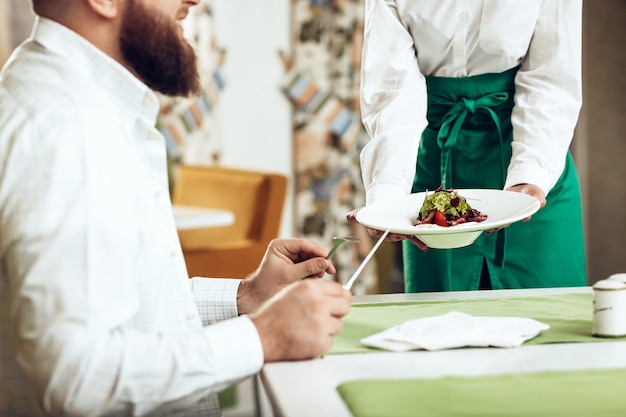 Il cameriere della ragazza serve il suo piatto nel ristorante a un uomo