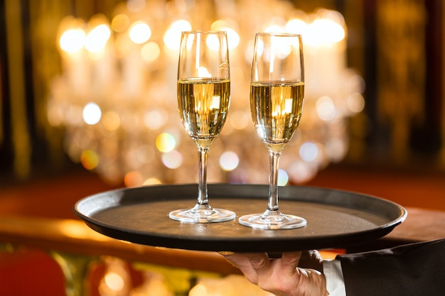 Il cameriere ha servito bicchieri di champagne su un vassoio in un raffinato ristorante, all'interno è presente un grande lampadario
