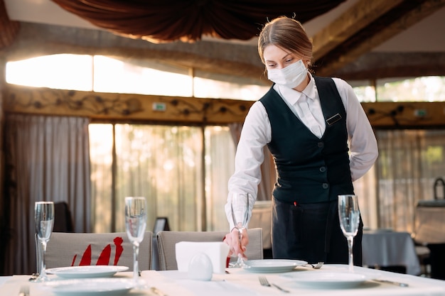 il cameriere in una maschera protettiva medica serve il tavolo del ristorante.