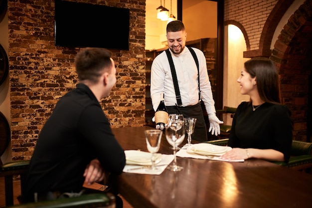 Il cameriere in uniforme offre ai visitatori del vino al ristorante