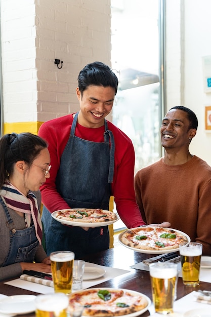 Il cameriere serve la pizza a un gruppo di amici in un bar con bicchieri da bere sul tavolo