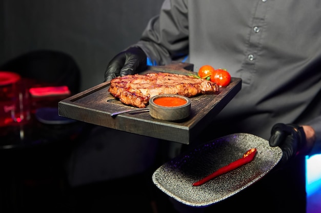 Il cameriere tiene in mano un piatto con bistecca con salsa di pomodori e peperoncino