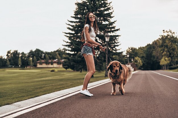 Il cane la rende felice! Per tutta la lunghezza della bella giovane donna che gioca con il suo cane e sorride mentre trascorre del tempo all'aperto