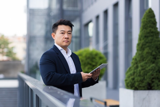 Il capo asiatico serio legge le notizie dal tablet vicino all'uomo d'affari maschio dell'ufficio moderno in giacca e cravatta