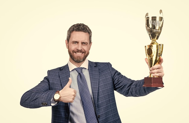 Il capo felice tiene la tazza d'oro che dà i pollici in su gesto della mano isolato su bianco migliore