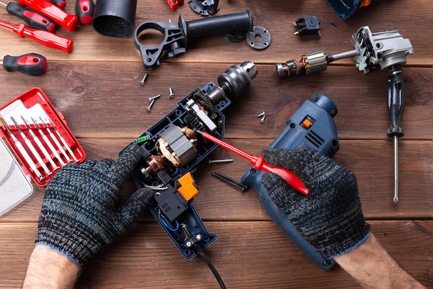 Il caposquadra ripara un apparecchio elettrico rotto: un trapano, una taglierina su un tavolo di legno. Officina di riparazione di utensili elettrici. Mano di un caporeparto che ripara un trapano.