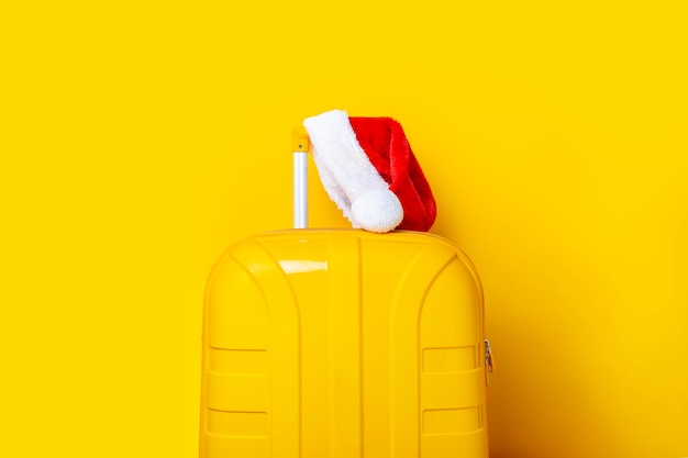 Il cappello di Babbo Natale giace su una valigia gialla su sfondo giallo.