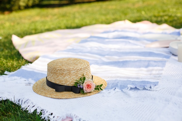 Il cappello di paglia con i fiori freschi giaceva su una coperta da picnic bianca al giorno di estate luminoso del prato inglese verde