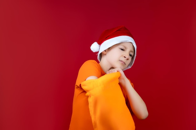 Il cappello natalizio di Babbo Natale che si erge su uno sfondo rosso ha infilato la mano in sacchetti regalo gialli