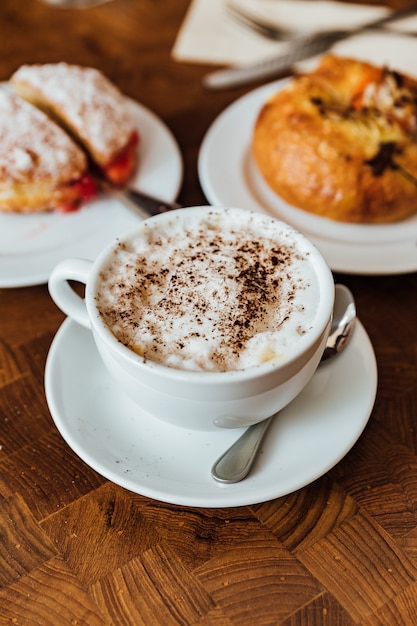 Il cappuccino caldo in vetro ceramico è servito sulla tavola di legno di mattina con pane.