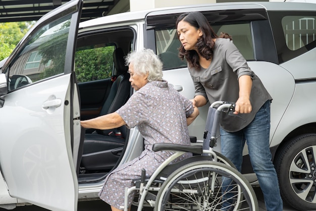 Il caregiver aiuta e sostiene una donna anziana asiatica seduta su una sedia a rotelle che si prepara ad arrivare alla sua auto per viaggiare in vacanza