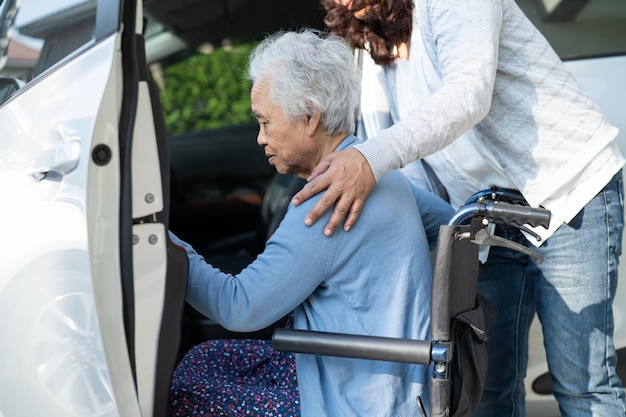 Il caregiver aiuta e sostiene una donna anziana asiatica seduta su una sedia a rotelle che si prepara ad arrivare alla sua auto per viaggiare in vacanza