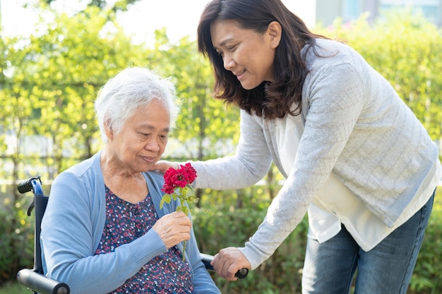 Il caregiver aiuta la donna anziana asiatica che tiene il sorriso del fiore della rosa rossa e felice