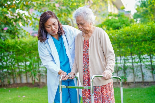Il caregiver aiuta la donna anziana asiatica con disabilità a camminare con il deambulatore nel concetto medico del parco