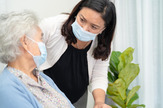 Il caregiver aiuta la donna anziana o anziana asiatica seduta su una sedia a rotelle e che indossa una maschera facciale per proteggere l'infezione di sicurezza Covid19 Coronavirus