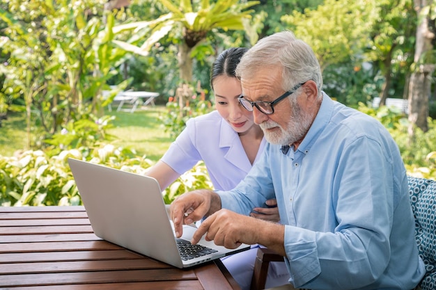 Il caregiver assiste il senoir uomo anziano che digita utilizzando il computer portatile del notebook per la connessione a Internet