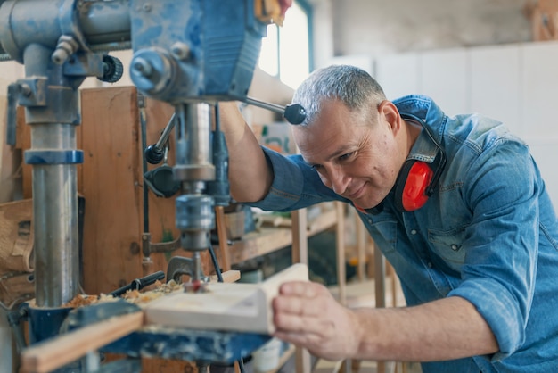 Il carpentiere maturo che per mezzo del trapano introduce l&#39;officina. Lavorazione del legno