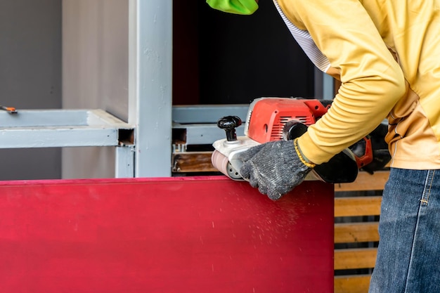 Il carpentiere sta radendo la porta di legno rossa dalla sua macchina da barba nel campo all'aperto