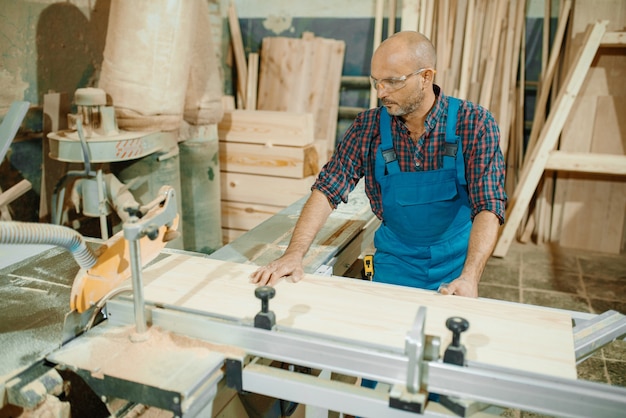 Il carpentiere taglia tavola di legno su sega circolare, lavorazione del legno, industria del legname, falegnameria.