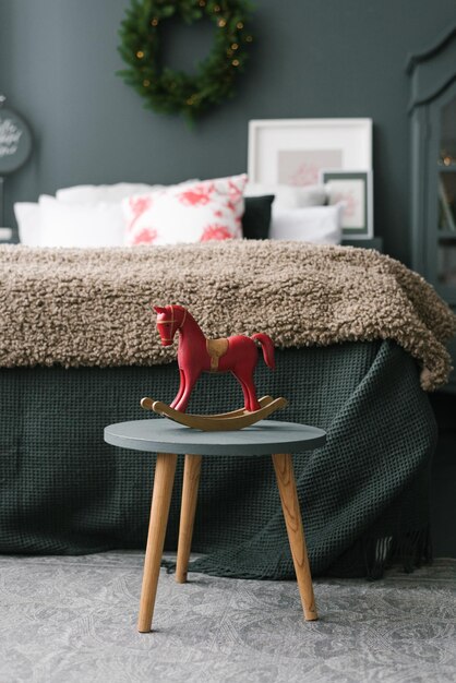 Il cavallo giocattolo in legno vintage si trova su uno sgabello nella camera da letto natalizia vicino al letto in colori scuri