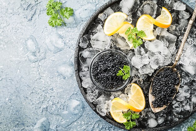 Il caviale nero in una ciotola di vetro su ghiaccio con il limone si chiuda sopra la vista superiore della superficie grigia