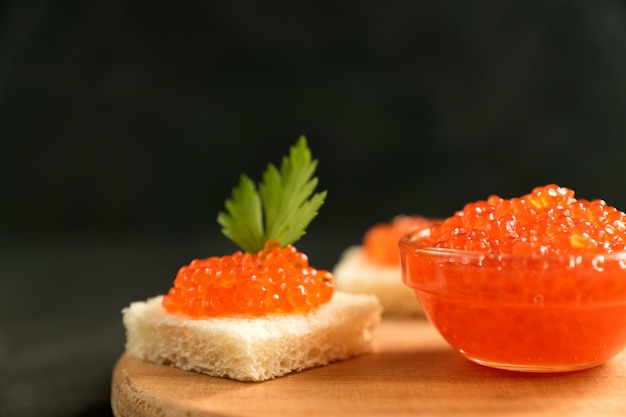 Il caviale rosso delizioso su pane integrale è servito con parseley sullo scrittorio di legno.