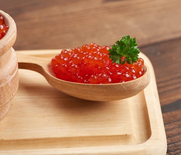 Il caviale rosso di salmone rosa giace in un cucchiaio di legno su un tavolo di legno marrone, primo piano