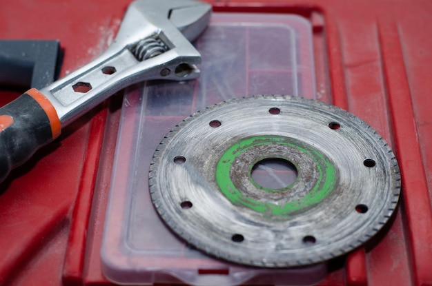 Il cerchio per la smerigliatrice e la chiave regolabile si trovano sulla cassetta degli attrezzi rossa. Operaio che si prepara per la riparazione nell'appartamento