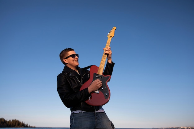 Il chitarrista in una giacca di pelle suona una chitarra elettrica rossa contro un cielo blu