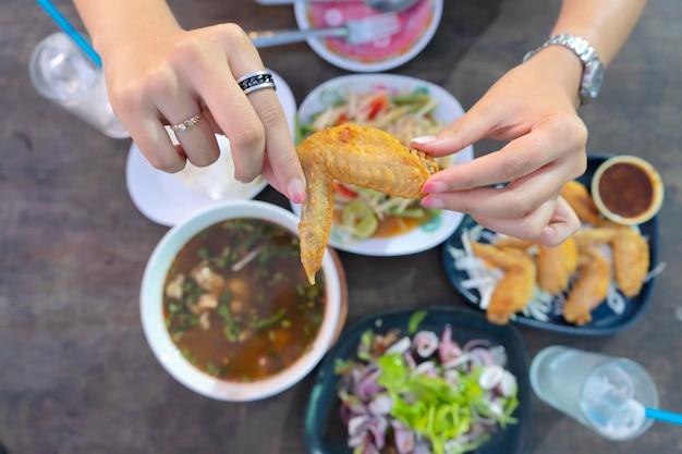 Il cibo tailandese è molto popolare tra le persone di tutto il mondo Le mani delle donne che catturano le ali di pollo fritte Il cibo tailandese e lo mangiano Sullo sfondo ci sono vari tipi di cibo