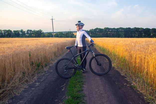 Il ciclista con la bici in un campo a guardare il tramonto. sport e hobby. attività all'aperto