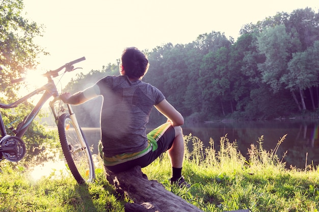 Il ciclista del ragazzo si siede e guarda lontano vicino al fiume