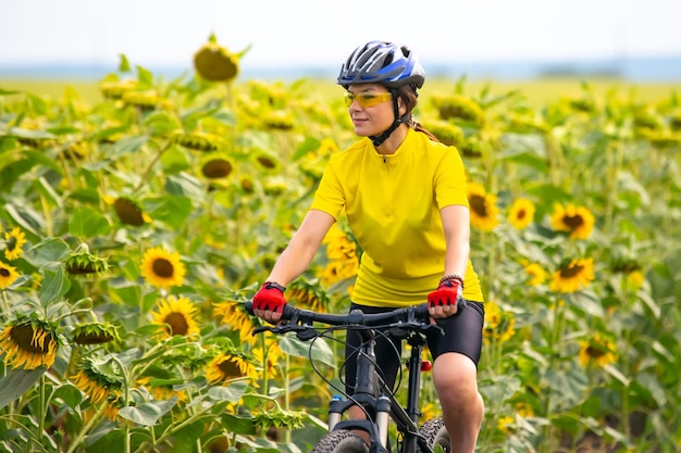 Il ciclista della bella donna guida un campo con i girasoli su una bicicletta Stile di vita sano e sport Tempo libero e hobby