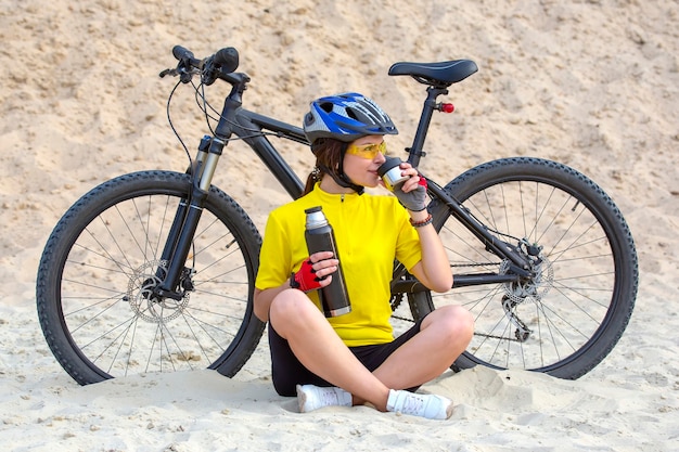 Il ciclista della bella ragazza versa il tè da un thermos