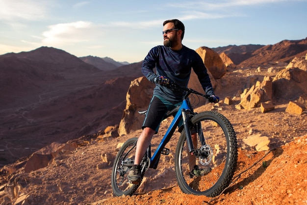 Il ciclista in pantaloncini e maglia su una moderna bici hardtail in carbonio con una forcella a sospensione pneumatica percorre fuoristrada sulle colline arancione al tramonto sera in estatex9xA