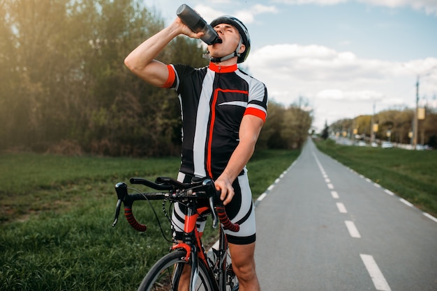 Il ciclista maschio in casco e abbigliamento sportivo beve l'acqua durante l'allenamento.