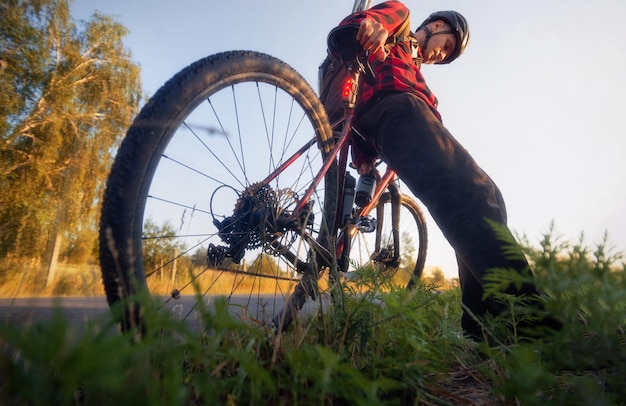 Il ciclista si siede sulla sua bicicletta vicino alla strada al mattino soleggiato Inquadratura dal basso