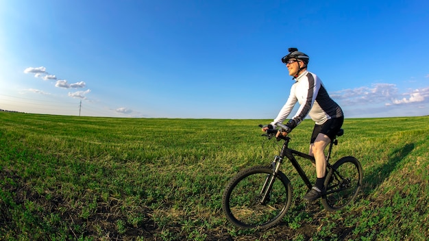 Il ciclista va in bicicletta sull'erba verde del campo. Sport all'aperto. Uno stile di vita sano.