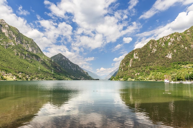 Il cielo blu si riflette nel Lago d'Idro alpino di alta montagna incorniciato da ripide scogliere, Lombardia, Italia