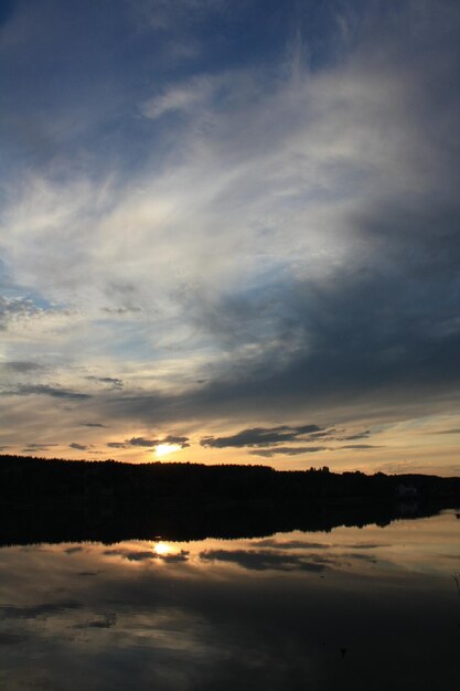 Il cielo nuvoloso al tramonto si riflette nella foto del paesaggio del lago della foresta