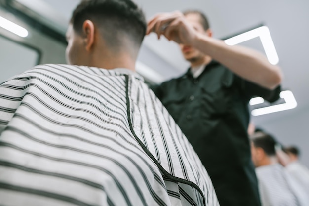 Il cliente in vestaglia fa un taglio di capelli in un barbiere un parrucchiere crea un'acconciatura maschile alla moda