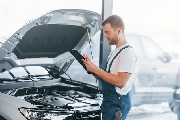 Il cofano è aperto Il giovane in camicia bianca e uniforme blu ripara l'automobile