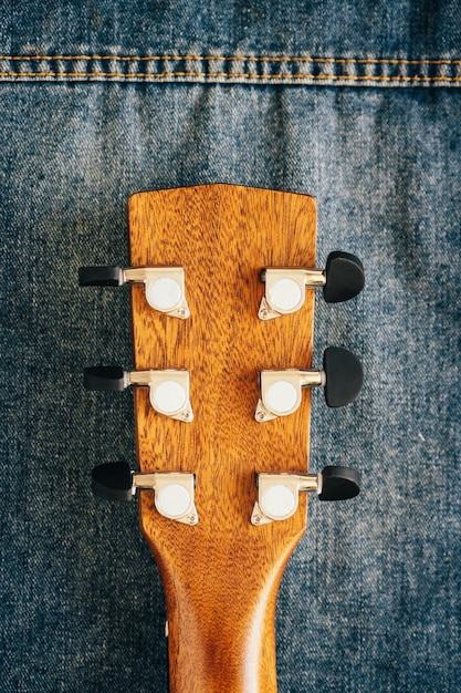 Il collo della chitarra acustica è primo piano su tessuto denim Cultura hipster Sfondo Strumento musicale