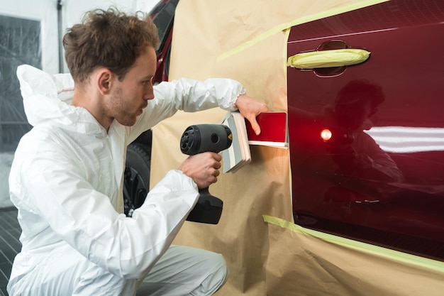 Il colorista maschio confronta il campione di colore con la vernice per auto utilizzando una lampada speciale