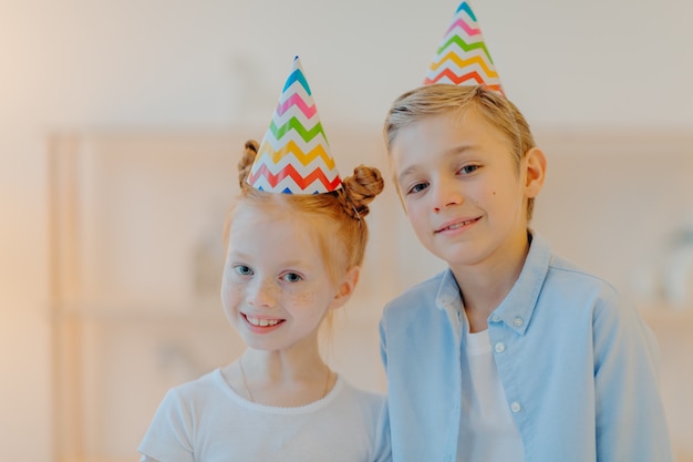 Il colpo orizzontale della ragazza e del ragazzo felici porta i cappelli del partito del cono, celebra insieme il compleanno