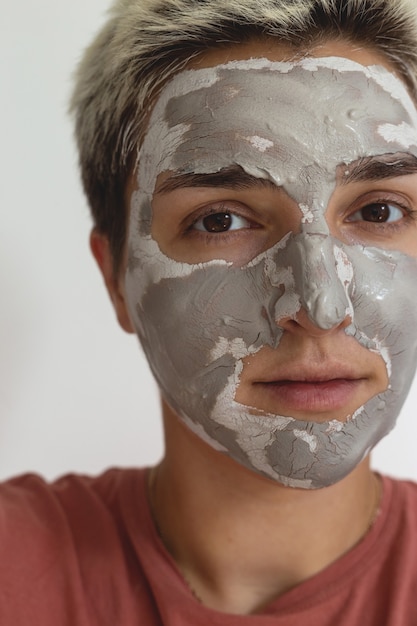 Il colpo ritagliato della donna applica la maschera di argilla per la cura della pelle verde grigia sulla routine quotidiana di cura della pelle di bellezza del viso