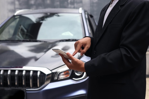 Il colpo ritagliato delle vendite del rivenditore di auto che indossa un abito sta utilizzando il tablet davanti all'auto.