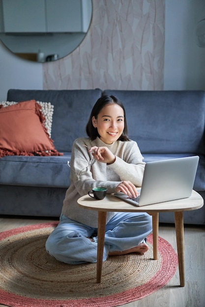 Il colpo verticale della ragazza asiatica si siede sul pavimento a casa lavorando su un computer portatile studiando in un luogo accogliente utilizzando com