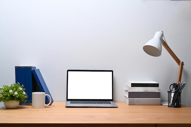 Il computer portatile di vista frontale libri la tazza di caffè della lampada una pianta d'appartamento sulla tavola di legno