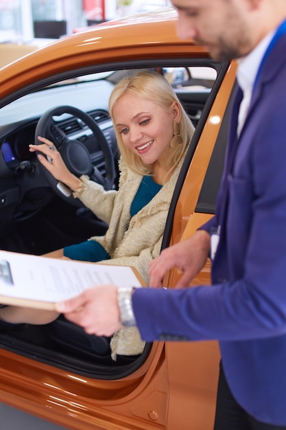 Il concessionario con una donna si trova vicino a un'auto nuova nello showroom